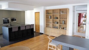 A modern kitchen with a central island, bar stools, and built-in ovens. - 3-bedroom house (Les Mages)