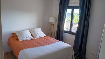 Quarto com cama, luminária e janela com cortinas.