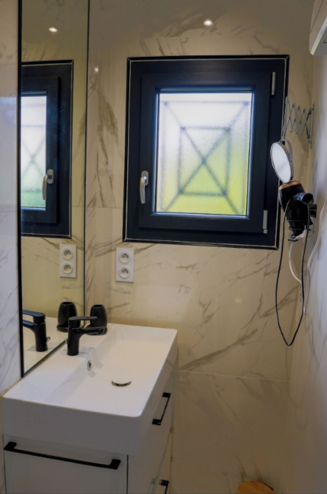 A bathroom with a white sink, a mirror, a window with a geometric pattern, and a towel rack.