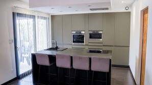 A modern kitchen with a central island, bar stools, and built-in appliances. - 3-bedroom house (Les Mages)