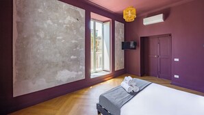 Ein Schlafzimmer mit großem Fenster, einem Bett mit aufgerollten Handtüchern, einem Fernseher und einer Tür.