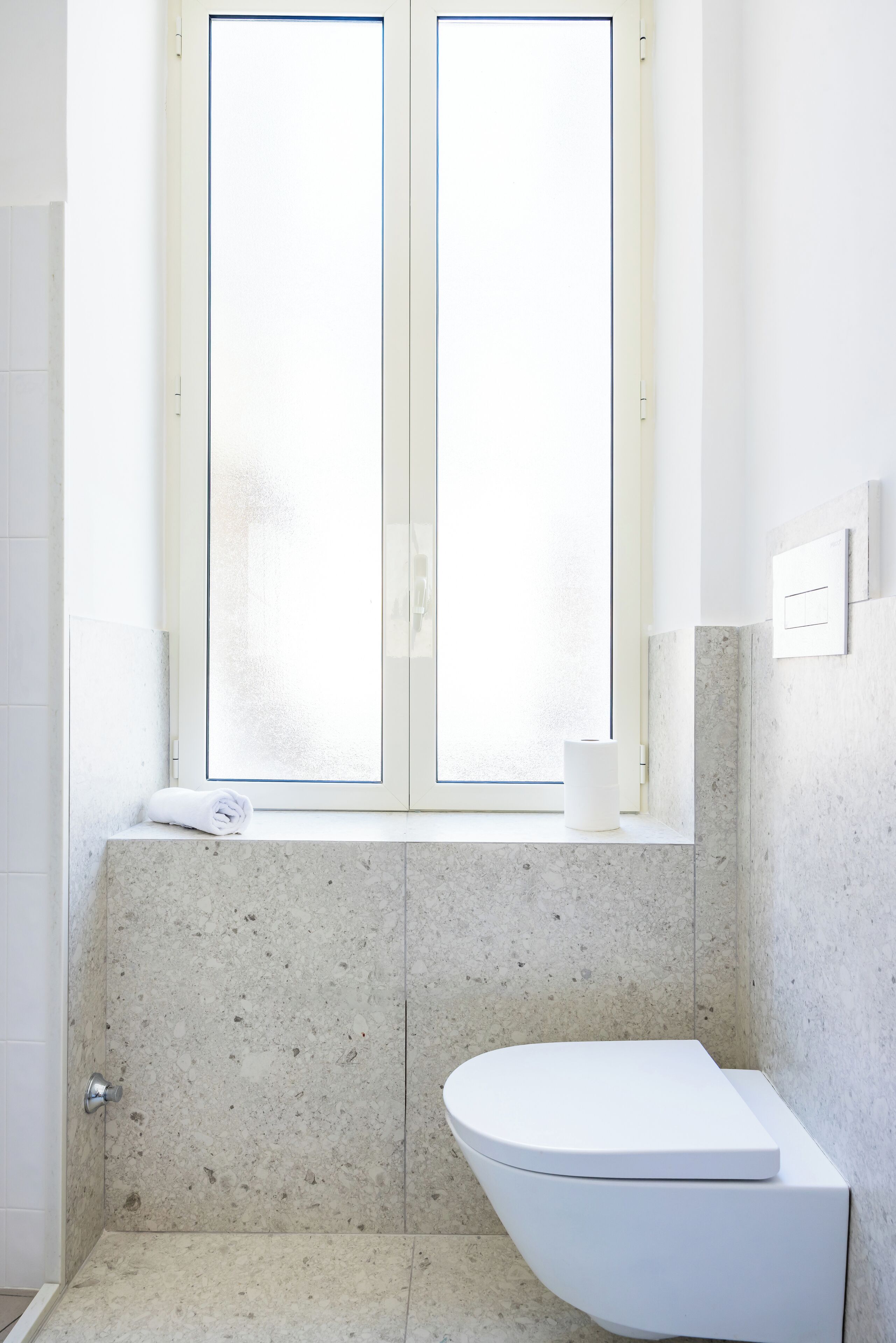 Ein Badezimmer mit Toilette, einem Fenster und einem Handtuch auf dem Ablageregál.