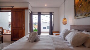 A bedroom with a large bed, a wooden door, a view of the outside, and a hanging light fixture. - Romansa Canggu (Canggu)