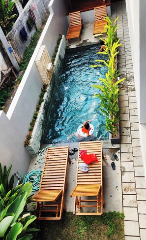 Une piscine dans laquelle une personne flotte sur un flotteur, entourée de meubles en bois et de plantes.