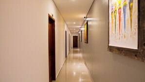 A hallway with a polished floor, wooden doors, and framed artwork on the walls. - Romansa Canggu (Canggu)