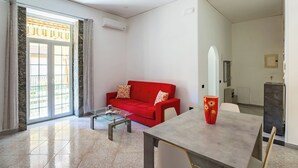 Un salon avec un canapé rouge, une table basse en verre et une table à manger agrémentée d’un vase.