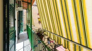 Un couloir étroit avec des volets verts, un pot de fleurs et un auvent rayé.