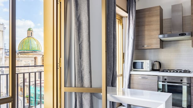 A modern kitchen with a view of a dome building, a dining area, and a balcony with curtains. - Revolutionary Apartment Near Duomo Station (Naples)