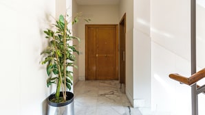 Un couloir avec une plante en pot, une porte en bois et un sol en marbre.