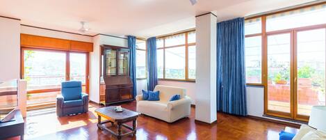 A spacious living room with a wooden floor, a white sofa, a blue armchair, a coffee table, and a ceiling fan.