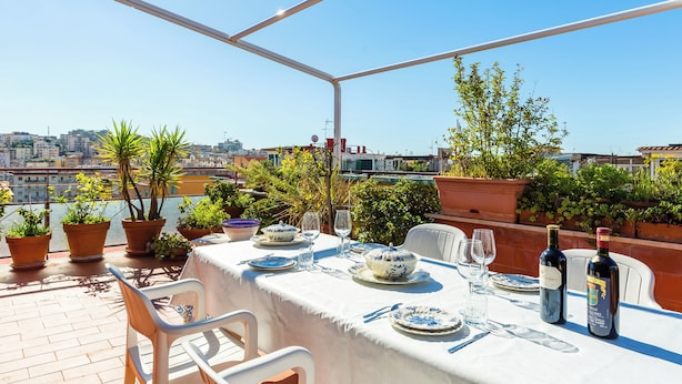 Une terrasse sur le toit, avec une table dressée pour le dîner, des plantes en pot et une vue sur la ville.