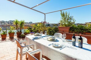 A rooftop terrace with a table set for dining, potted plants, and a city view. - Terrazza 30 by Napoliapartments (Naples)