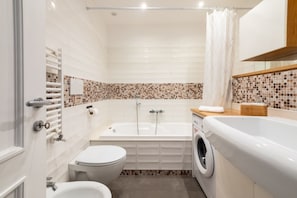 A bathroom with a bathtub, toilet, and washing machine.