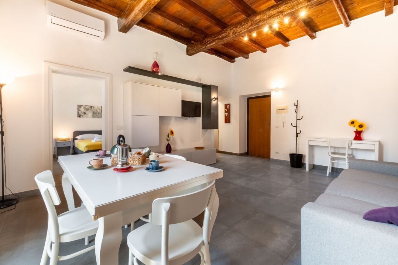 Un salon moderne avec un canapé blanc, une table à manger avec des chaises, un coin cuisine et un plafond en bois.