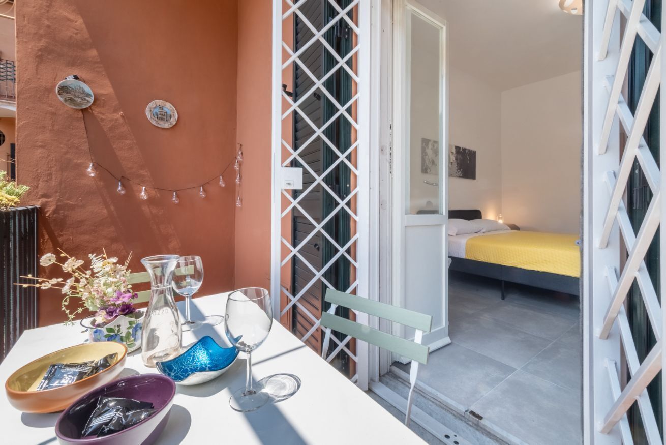 Un balcon avec une table mise, comprenant des verres, un vase de fleurs et un saladier.