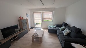 Una sala de estar moderna con un televisor de pantalla plana, muebles de madera, un sofá negro y un puerta corrediza de vidrio que da a un jardín.
