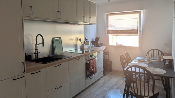 Una cocina moderna con armarios blancos, un fregadero y un comedor con sillas y una mesa de madera.