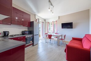 A modern kitchen with red cabinets, a dining area with a table and chairs, and a red sofa. - Sole Mare by Wonderful Italy (Sanremo)