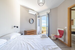 Un dormitorio con cama, cómoda, silla roja, radiador y balcón con vistas.