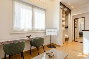 A modern hotel room with a marble desk, two chairs, a glass table, a large window with sheer curtains, a wardrobe, and a mirror. - Mercantile 76 - Elegant Loft in the Historic Center (Bari)