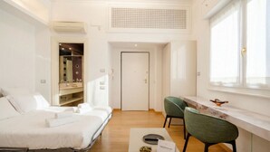 A modern hotel room with a bed, a seating area with chairs, a small table with snacks, a window, and a door.