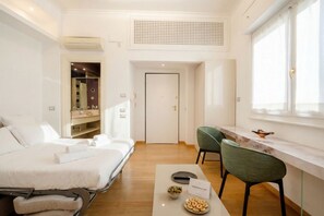 Een moderne hotelkamer met een bed, een zithoek met stoelen, een tafeltje met hapjes, een raam en een deur.