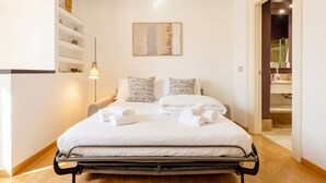A neatly made bed with white linens and pillows, a bedside lamp, and a painting on the wall.