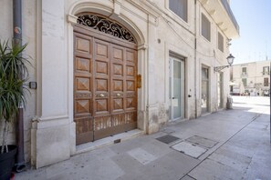 A building with a large wooden door, a small window, and a potted plant on the sidewalk. - Mercantile 76 - Elegant Loft in the Historic Center (Bari)