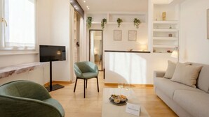 A modern living room with a sofa, a green armchair, a TV, and a dining area with a table set for two.