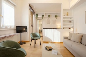 Een moderne woonkamer met een bank, een groene fauteuil, een televisie en een eethoek met een tafel gedekt voor twee personen.