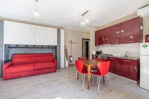A modern kitchen with red cabinets, a dining table with four red chairs, and a red sofa in a living area.