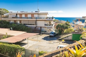 A residential area with a view of the sea, featuring a building with a balcony and a parked car.