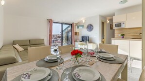 A dining area with a table set for four, a sofa, a TV, and a kitchen area with a microwave. - 3 bedroom lovely apartment in Medulin (Medulin)