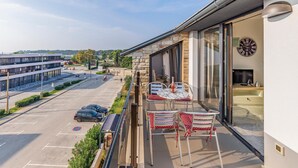 A balcony with two tables and chairs, a clock, and a view of a parking lot and buildings. - 3 bedroom lovely apartment in Medulin (Medulin)