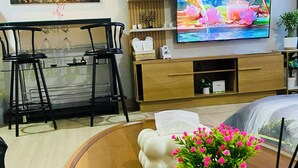 A modern living room with a wooden dining table, black chairs, a flat-screen TV, and a decorative vase with pink flowers. - SMDC Park Residences Condo unit 417 near SM City of Santa Rosa Laguna (City of Santa Rosa)