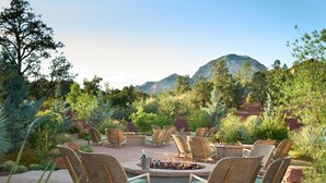 Un espace extérieur aménagé avec des chaises en osier et un foyer, entouré d’une végétation luxuriante et avec des montagnes en toile de fond.