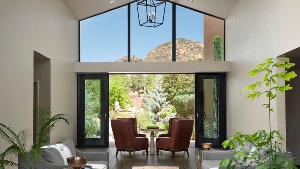Un vaste espace de vie doté d’un haut plafond, de grandes fenêtres et d’une vue sur un jardin. On y trouve deux canapés, une table basse et une table à manger avec des chaises.