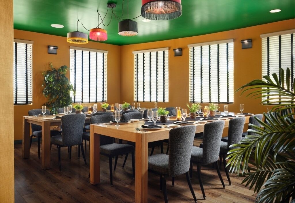 Een eethoek met een houten tafel, gedekt voor een maaltijd, omringd door stoelen, grote ramen en planten.