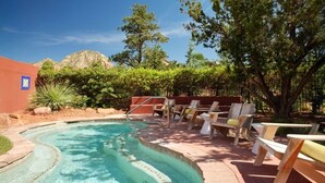 Una piscina con diseño curvo, rodeada de sillas y mesas de madera, con árboles y una montaña al fondo.