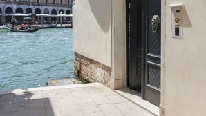 A building with a black door, a balcony with white railings, and a view of a canal with boats. - Ca Dadda terrace at Rialto Bridge -historic residence equipped with all comforts (Venezia)
