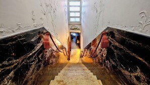 A grand staircase with marble walls and a chandelier, leading to a room with a large window. - Ca Dadda terrace at Rialto Bridge -historic residence equipped with all comforts (Venezia)