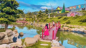 Un jardín tranquilo con un estanque, un puente rojo y un edificio de techo verde.