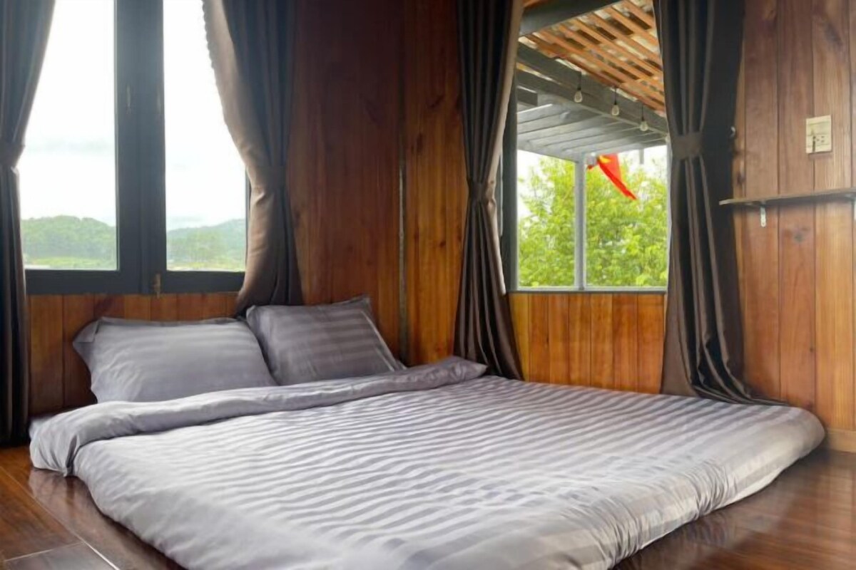 A wooden room with a bed, large windows, and curtains.