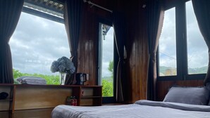 Un dormitorio con una cama, una estantería con un jarrón y una taza, y vistas al verdor exterior.