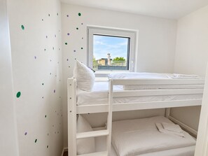 A bunk bed room with a window, white walls, and a view of buildings outside.