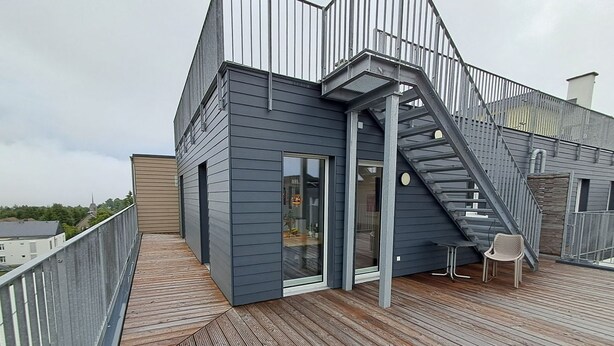 Ein modernes Gebäude mit einer Holzterrasse, einer Treppe und einer Glastür zu einem Innenbereich.