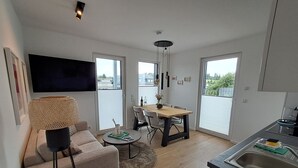 Ein modernes Apartment mit Sofa, Esstisch, Fernseher und Küchenbereich.