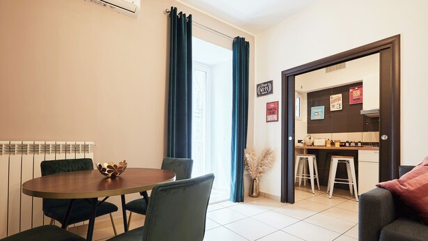 A dining area with a round table and chairs, a kitchen area with stools, and a sofa. - Vicky's Luxury Guesthouse by Napoliapartments (Naples)