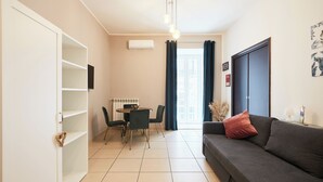 A modern living room with a sofa, a dining table with chairs, a white wardrobe, and a ceiling light fixture. - Vicky's Luxury Guesthouse by Napoliapartments (Naples)
