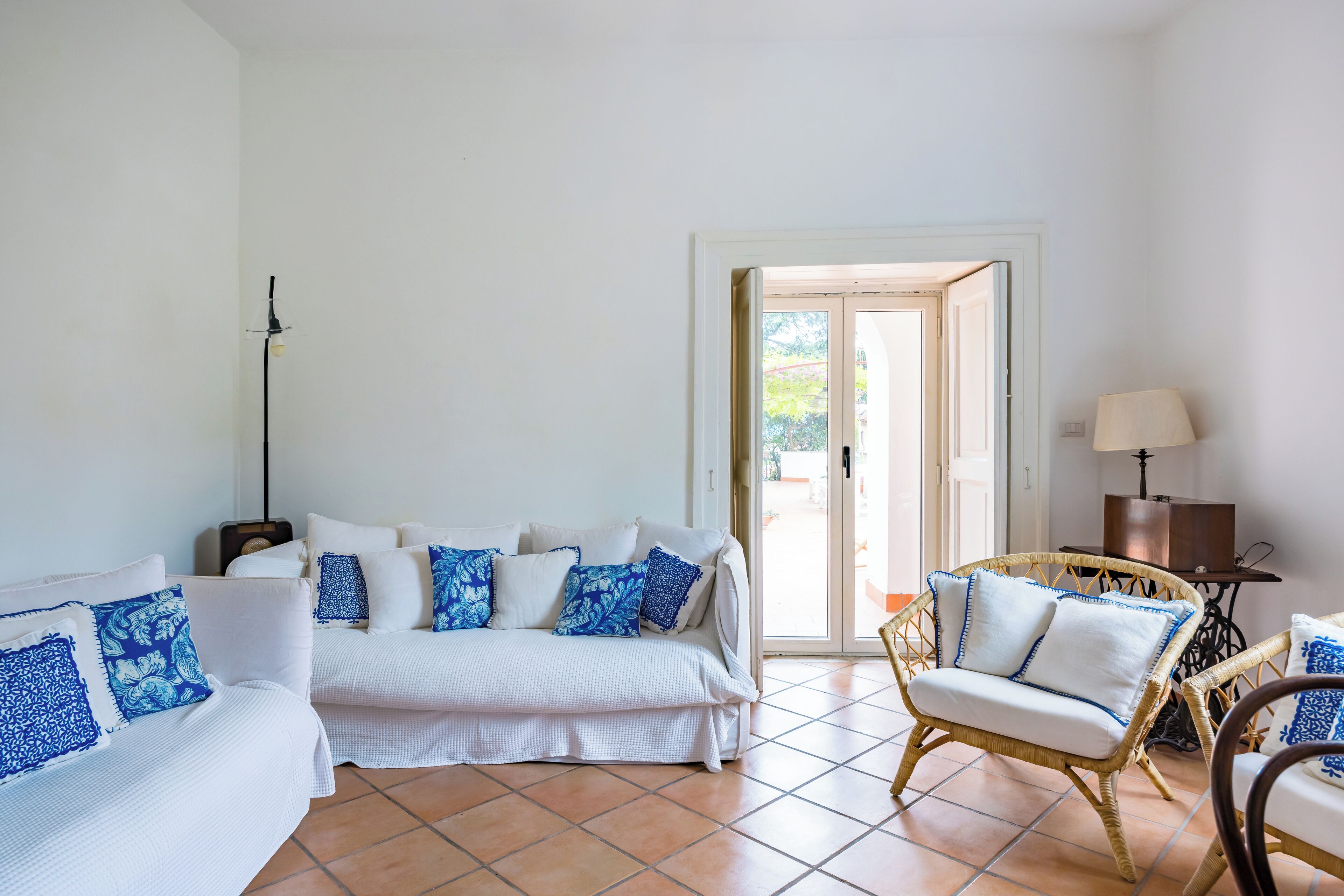 Une pièce avec un canapé blanc, un fauteuil en osier et une lampe.